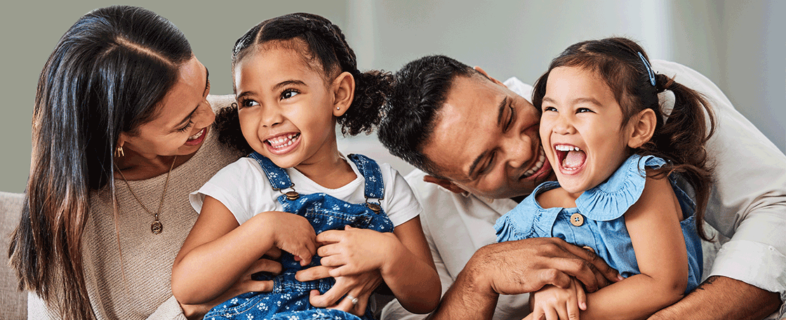 Happy family of four with parents and two kids sitting on a couch.