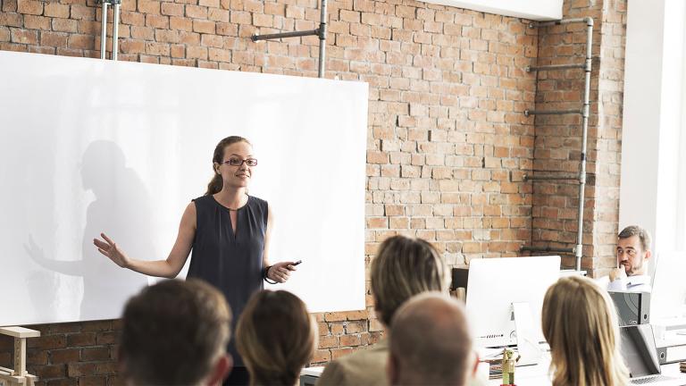 A group of people in a classroom setting, with a presenter standing.