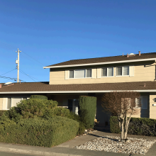 Beige Novato home with shrubs decorating the front lawn.